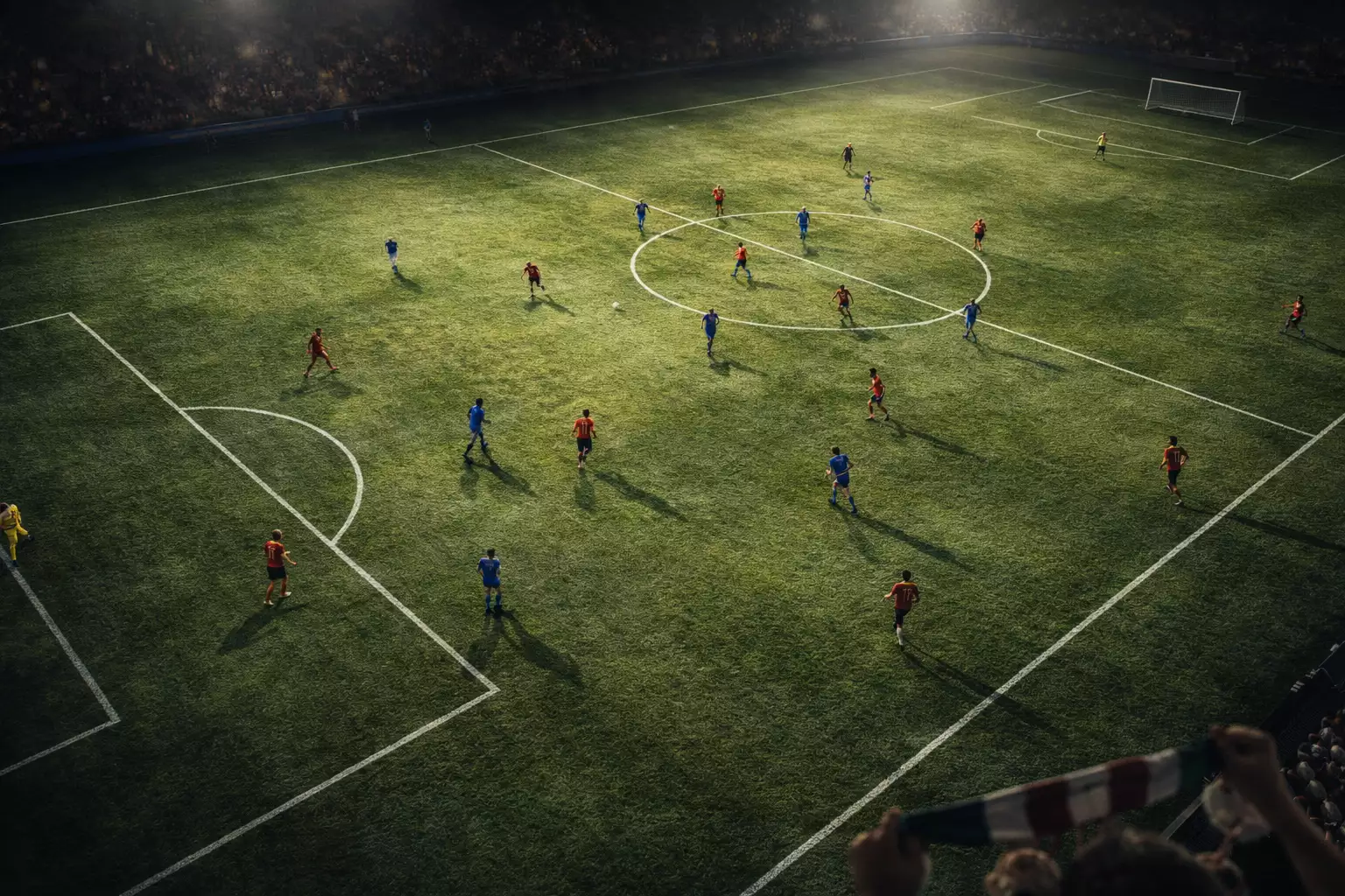 Campo di calcio visto dall'alto con i giocatori in azione durante una partita serale